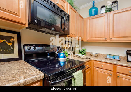 A kitchen features granite countertops, wooden cabinets, a glass cooktop stove, and a microwave at Cypress Cove Apartment Homes in Mobile, Alabama. Stock Photo