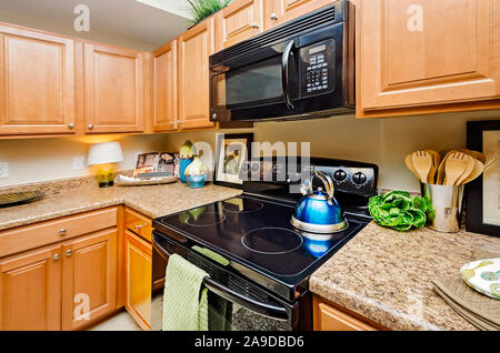 A kitchen features granite countertops, wooden cabinets, a glass cooktop stove, and a microwave at Cypress Cove Apartment Homes in Mobile, Alabama. Stock Photo