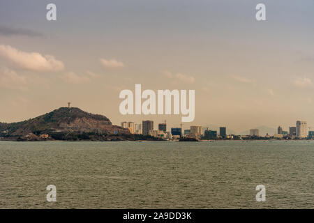 Vung Tau, Vietnam - March 12, 2019: Skyline of the city with high rise buildings adjacent to forest covered hill with on top giant Jesus Christ statue Stock Photo