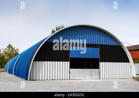 Close-up of the national flag of Estonia  painted on the metal wall of a large warehouse the closed territory against blue sky. The concept of storage Stock Photo