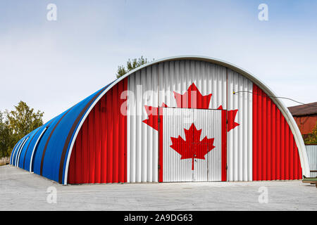 Close-up of the national flag of Canada  painted on the metal wall of a large warehouse the closed territory against blue sky. The concept of storage Stock Photo