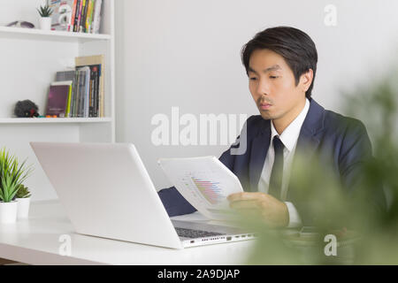 Asian Financial Advisor or Asian Consulting Businessman Analyze Financial Report in front of Laptop. Asian financial advisor or Asian consulting busin Stock Photo