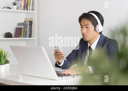 Asian Man Call Center Contact with Customer by Smartphone and Laptop. Asian man call center answers the customer question in front of laptop in office Stock Photo