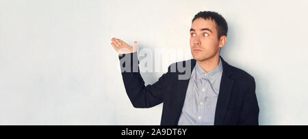 A young man in a jacket points to an empty blue wall. Mocap for design. Presentation display. blank Stock Photo