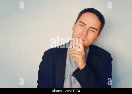 Thoughtful handsome male. A young businessman in a thoughtful pose reflects on business. Thinking through ideas and plans. A grown guy on a blue backg Stock Photo