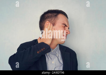 Young man suffering from Pain in right ear, over blue background. Medical concept. Diseases of the ear. Inflammation in the ear. Stock Photo
