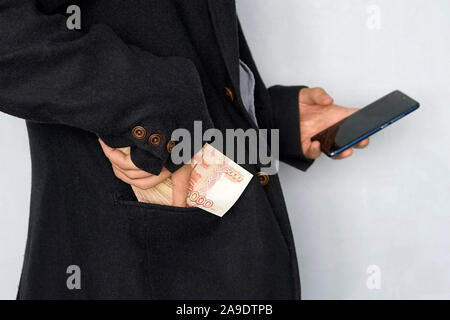 young man holds the money in his hand and presses the screen of the smartphone. Earns money through the mobile app. Business via smartphone. Stock Photo