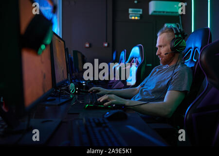 Young man wearing modern headphones sitting in front of computer monitor and typing on computer keyboard in computer class Stock Photo