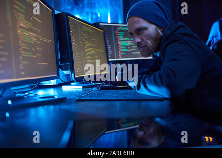 Serious computer hacker in dark clothing working in dark office he breaking the system on computers Stock Photo