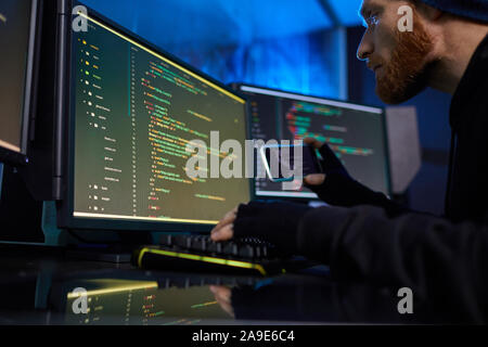Bearded computer hacker using mobile phone to break the computer system and stealing the information Stock Photo