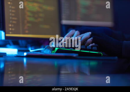 Close-up of man wearing black gloves typing on computer keyboard at the table in dark office Stock Photo