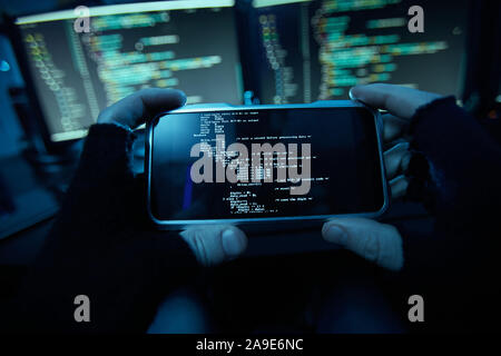 Close-up of computer hacker in black gloves holding his mobile phone and installing the new software on it in dark room Stock Photo