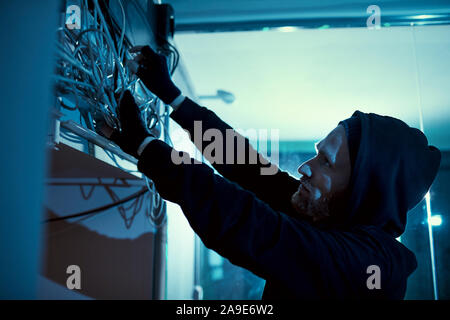 Electrician in black hoody shirt holding wires and trying to repair the electricity in the room Stock Photo