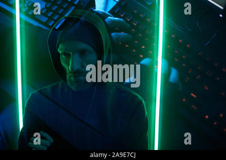 Computer hacker standing and remembering the password from computer system in dark room with green lights Stock Photo