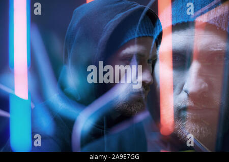 Blurred motion of young bearded man in black hoody shirt standing in dark room Stock Photo