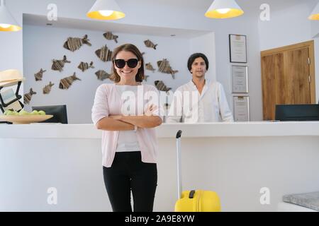 Portrait of female guest with suitcase, male hotel worker near reception Stock Photo