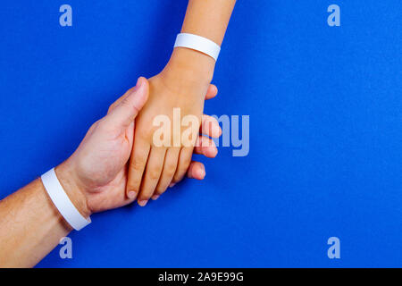 Mockup template blank paper wristband, bracelet on man and kid arms, blue color background Stock Photo