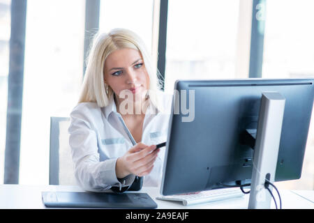 Professional photographer sitting at her office desk looking away and smiling. Stock Photo