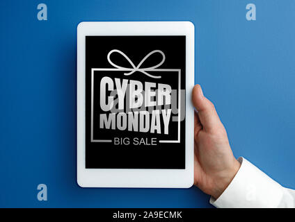 Male hand holding tablet with cyber monday words on blue background. Tech, modern, gadgets, business and advertising. Black friday, cyber monday, sales, finance, money online purchases concept. Stock Photo