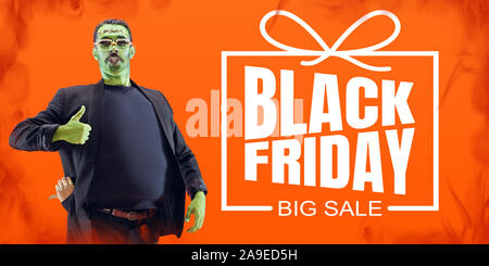 Man as a zombie with green skin and thumb up on orange fire background, black friday. Scary characters, business, advertising. Black friday, cyber monday, sales, finance, money online purchases concept. Stock Photo