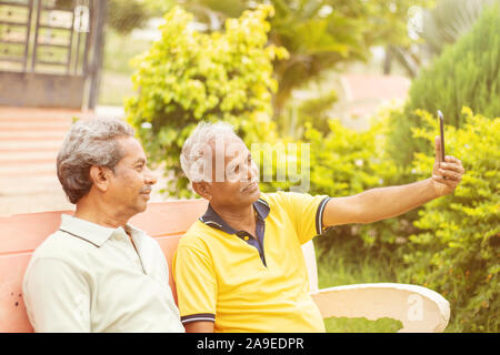 Two Senior happy friends taking a selfie at Park, Outdoor - Elderly men making Video call - Concept of active and fun elderly people using new Stock Photo