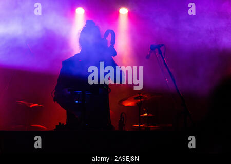 silhouette of a DJ during a musical performance at night, as he holding headphone and using electronic music equipment with lights and smoke in the background Stock Photo