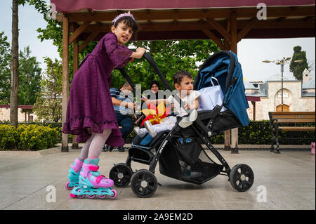 Girl playing with her brother, parents in the background near the Fatih Mosque, Istanbul, Turkey Stock Photo