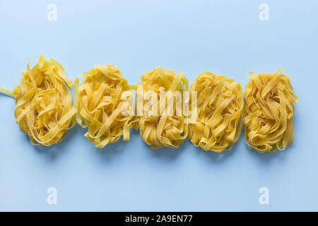 Raw egg pasta shape reginella rolled up by portion on blue. Isolated. View from above. Stock Photo