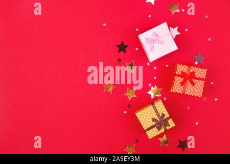 Three little boxes with gifts for the New Year or Christmas among gold stars on a bright red background. Black friday concept. Stock Photo