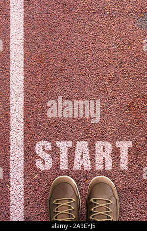 Feet and brown shoes with word start written on rubber sports track background. person standing on competition road with white race line beginning ide Stock Photo