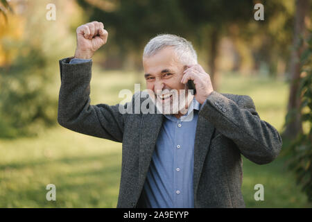 Happy elderly man speak with somebody by the phone. Handsome senior man with beautiful beard smile and rejoice Stock Photo