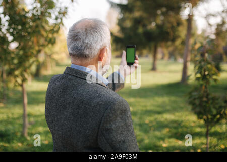 Mock up of elderly man using phone outside. Green screen. Back view of man holding phone at harm's length Stock Photo