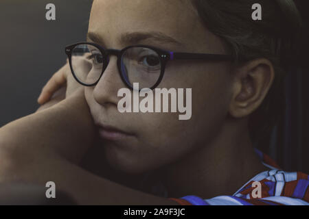 Portrait of a boy looking out of a car window in an evening ride in the city. Young male with eyeglasses looking away leaning on his arms. Soft focus Stock Photo