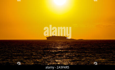 Silhouette of a big ship moving at the horizon during a beautiful summer sunset on the ocean. Ferry boat navigate on the sea with sun going down in ba Stock Photo