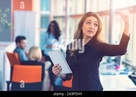 Portrait of happy businesswoman holding digital tablet in office standing in front of colleagues discussing at background Stock Photo