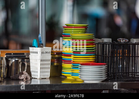 Stack of colourful clean dishes on stainless steel table. Urban outdoor cafe background Stock Photo