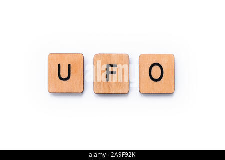 The abbreviation UFO which stands for Unidentified Flying Object, spelt with wooden letter tiles over a white background. Stock Photo