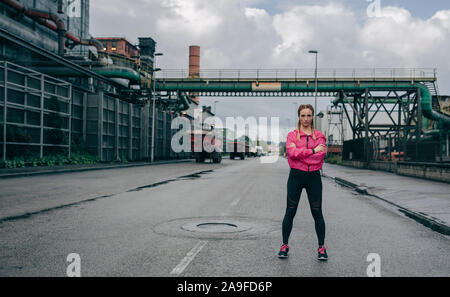 Sportswoman posing arms crossed in an industrial zone Stock Photo