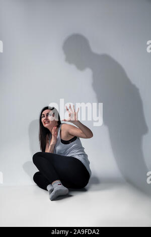 Woman in fear of domestic abuse, violence, concept of female rights. Stop agression. Shadow on the wall representing hidden sides of abusing, being victim of man, husband. Has bruises, hematomas. Stock Photo