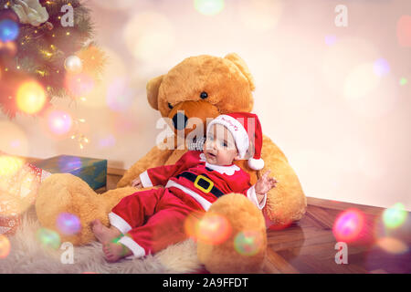 Little baby boy in Christmas Santa's costume with teddy bear  on Christmas day.Happy baby boy wearing santa clothes. Stock Photo