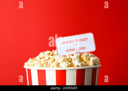 Striped bucket with popcorn and tickets against red background Stock Photo