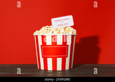 Striped bucket with popcorn and tickets against red background Stock Photo