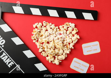 Heart laid out from popcorn, clapperboard and tickets on red background, top view Stock Photo