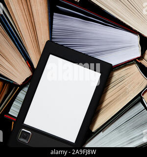 The e-book with a white screen lies on the open multi-colored books that lie on a dark background, close-up Stock Photo