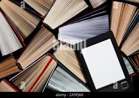 The e-book with a white screen lies on the open multi-colored books that lie on a dark background, close-up Stock Photo