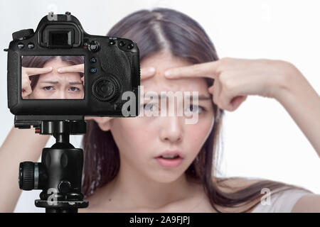 Asian American woman squeezing a spot on her forehead, social media concept Stock Photo