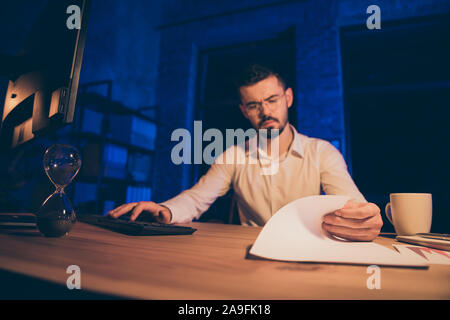 Photo of thoughtful serious student studying for exams at night with sandglass counting down time left till morning with cup of coffee nearby Stock Photo