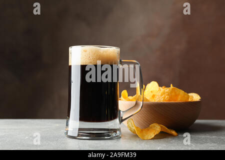 Glass of dark beer and chips on grey table, space for text Stock Photo