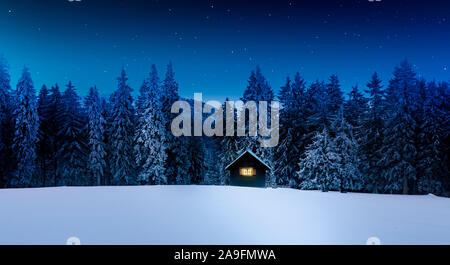 Log cabin with shining window in wintry forest Stock Photo