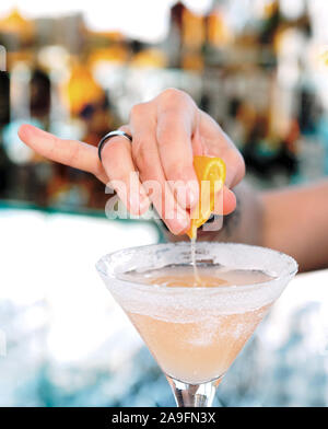 Female bartender is squeezing orange juice into a cocktail glass Stock Photo